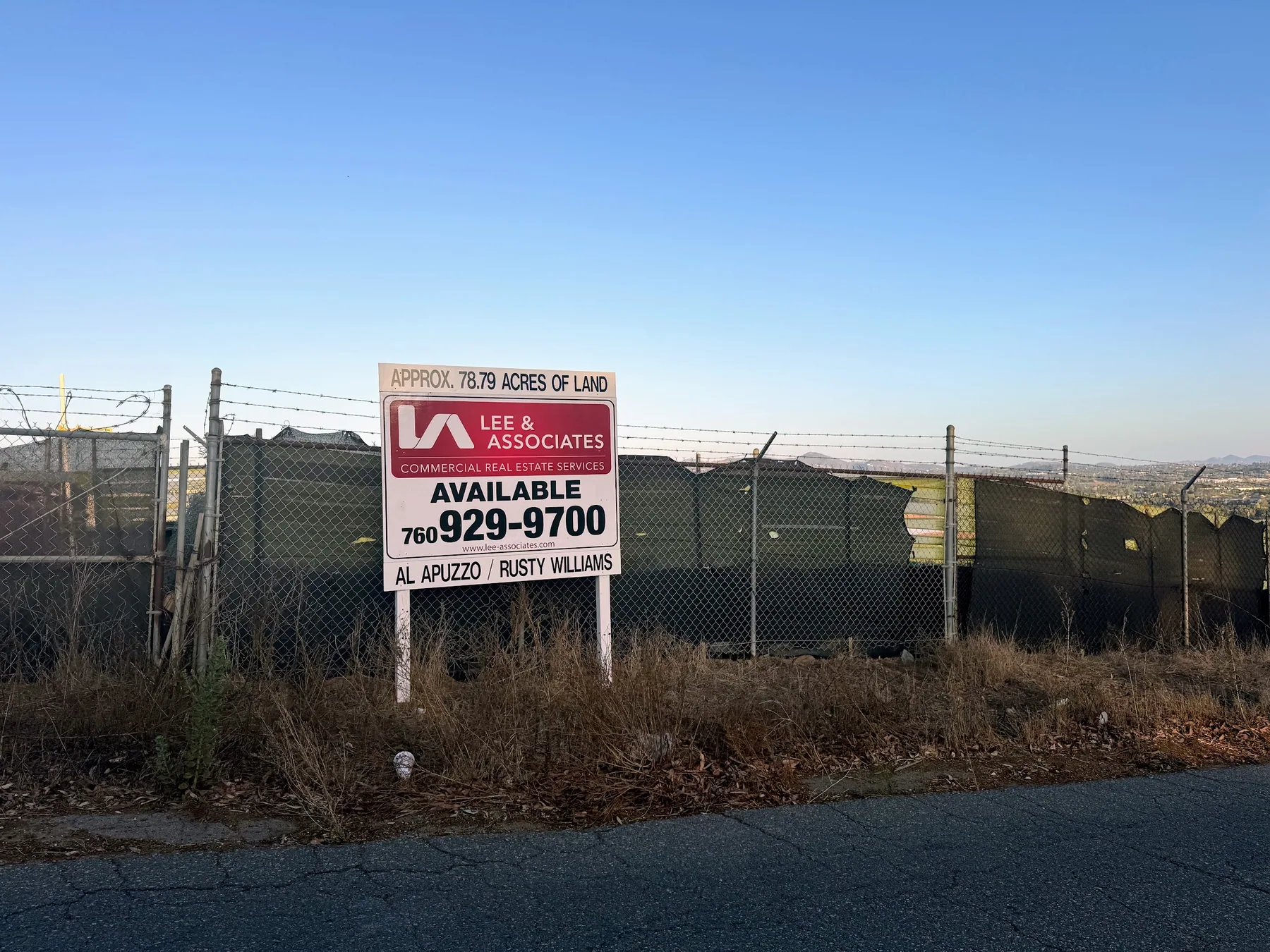 A commercial real estate sign reading "Approx. 78.79 acres of land, available" posted on the fence line of agricultural land in Oceanside.